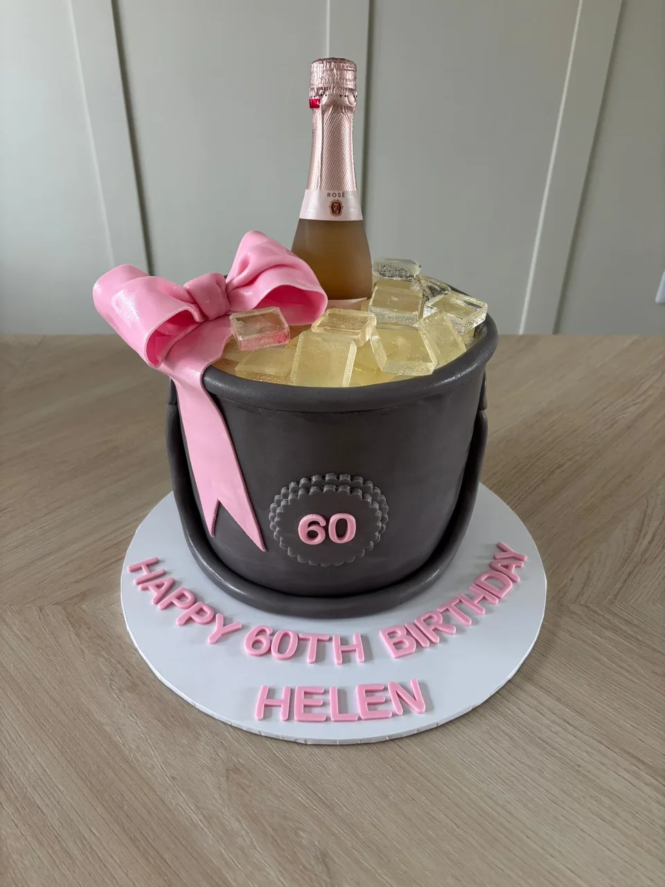 Black and gold champagne themed sixtieth birthday cake with a large pink bow