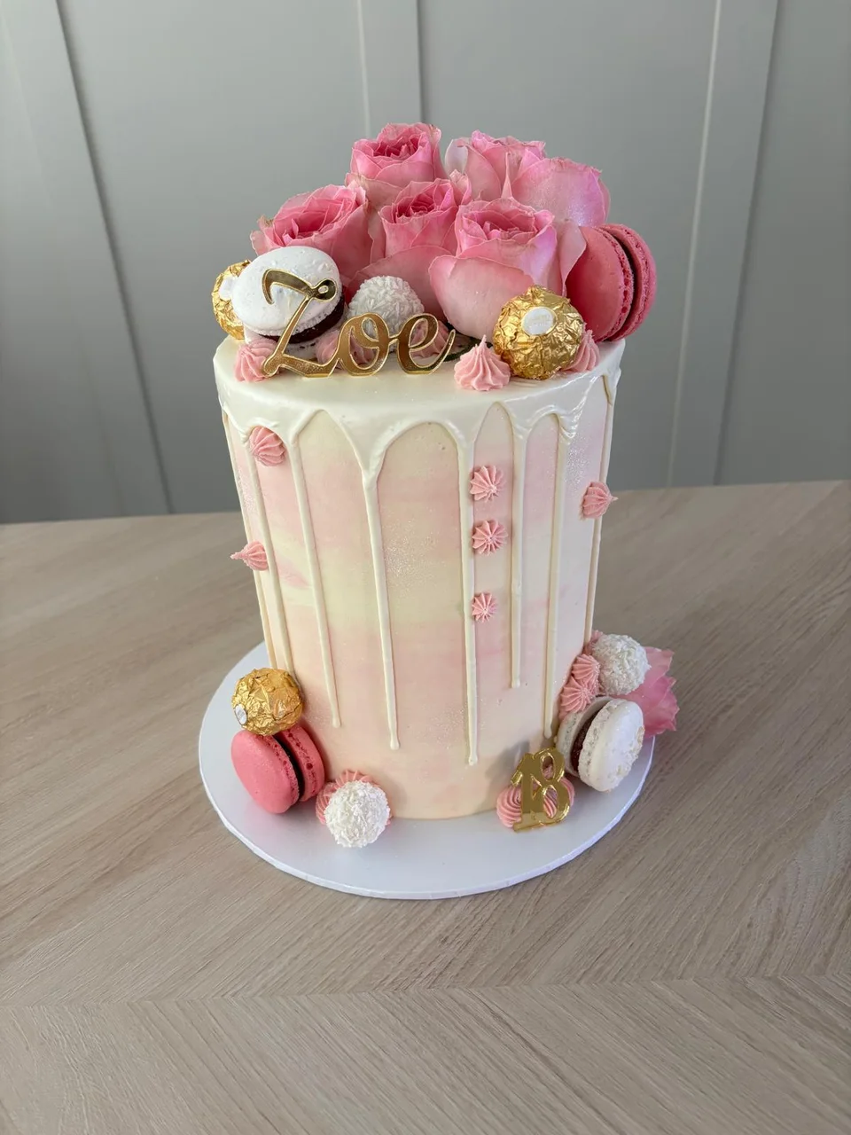 Tall pink drip cake decorated with buttercream roses, macarons and gold sweets